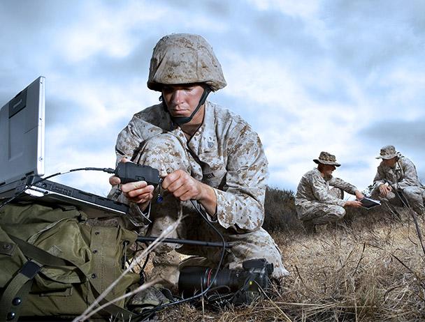 Three military soldiers in kneeling in 的 field, wearing camo and working on communications equipment